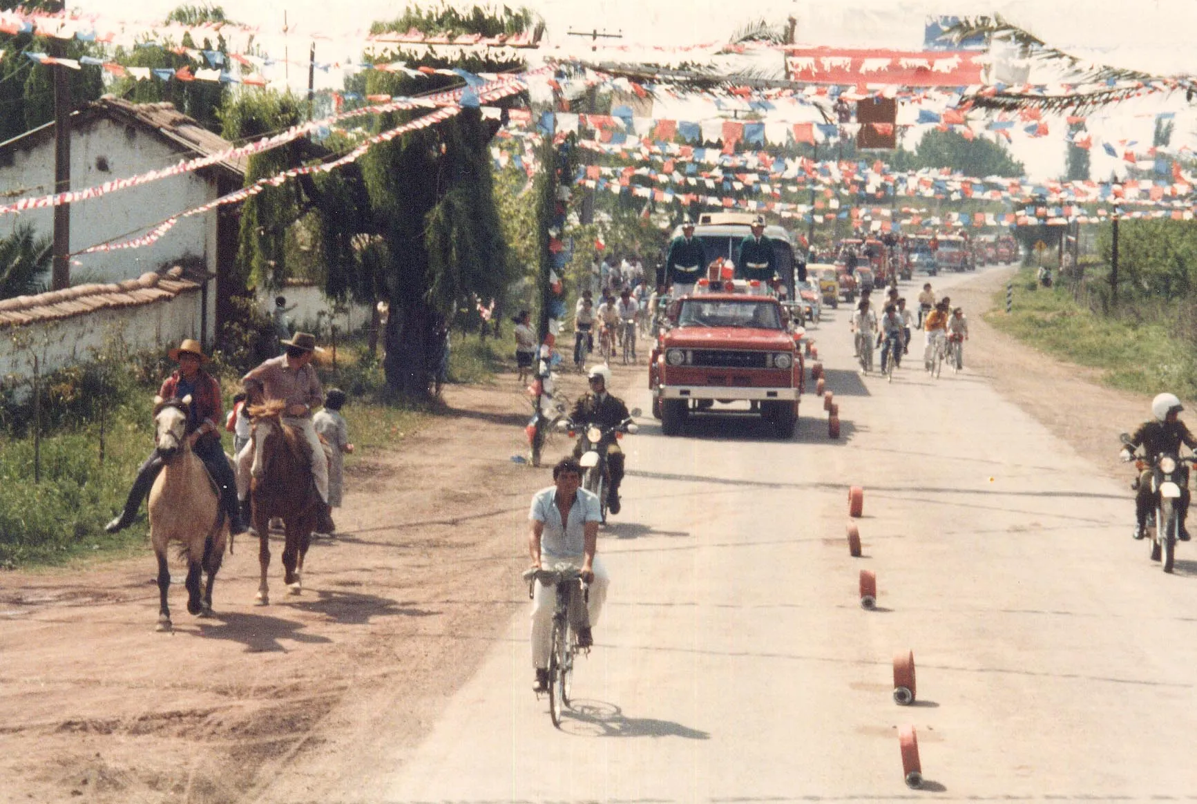 Fotografía histórica del camino al santuario engalanado con banderines, con peregrinos a caballo y en bicicleta