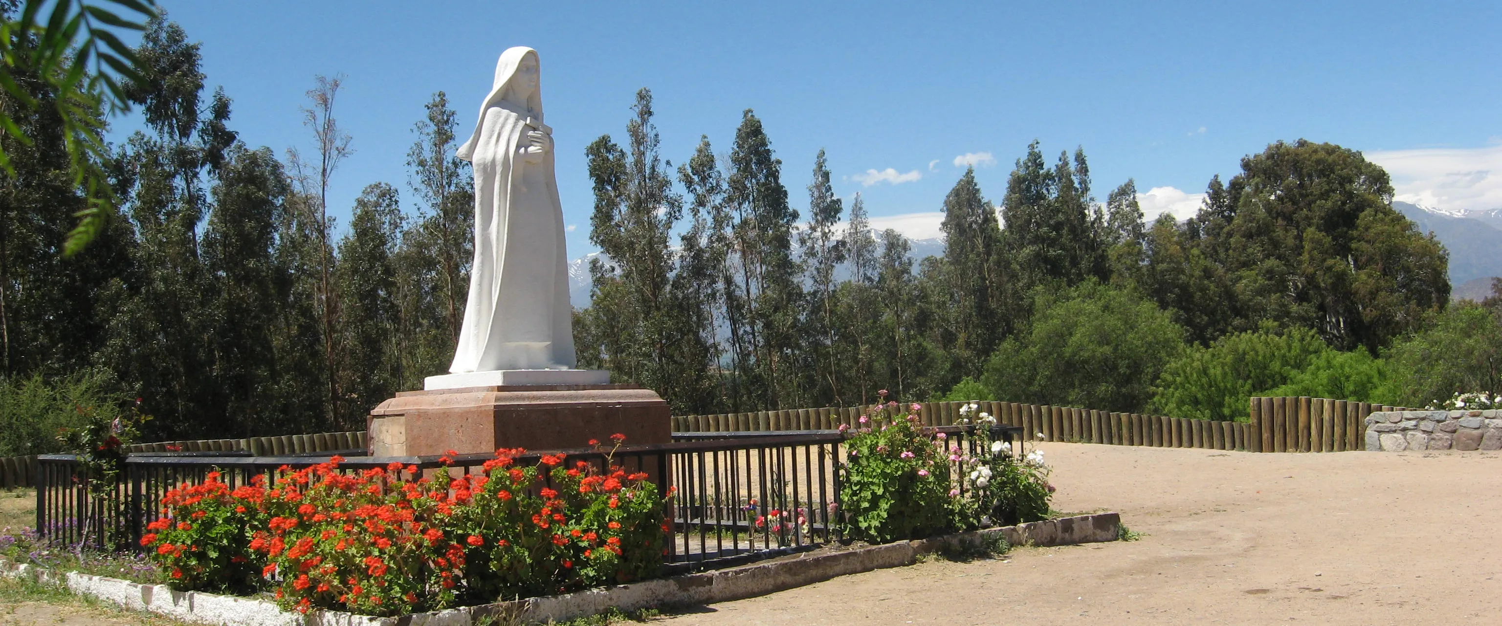Imagen externa de Santa Teresa: estatua blanca sobre un montículo, rodeada de flores